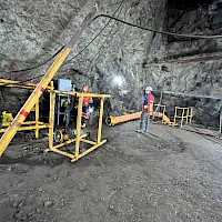 Promontorio - Balvanera shaft hoist room. Note yellow safety railing around Balvanera shaft collar at center-right of image and gray electrical control panel in center-left background. Orange air duct leads into shaft to provide ventilation. Steel casing slanting from right to left in left foreground contains electrical cable from for lighting and welding and other tools. The wooden beam above the shaft collar is a vestige of historical hoisting equipment.